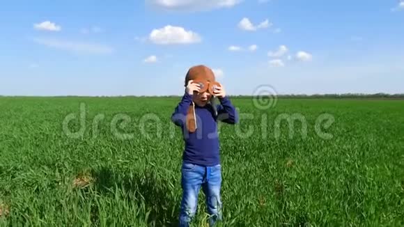 一个快乐的孩子站在绿色的田野上戴着飞行员的头盔顶着蓝天视频的预览图