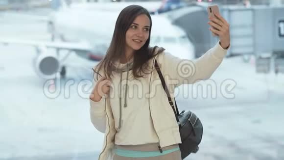 女孩自拍在机场的窗户附近显示拇指向上的手势和眨眼视频的预览图
