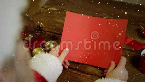 带着红色卡片的圣诞老人在书桌上撒着雪花的视频构图视频的预览图
