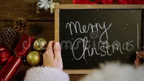 带着圣诞快乐的圣诞老人拿着黑板在桌子上撒着雪花的视频组合视频的预览图
