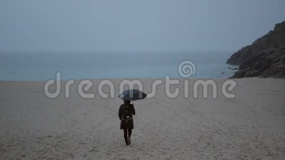 一个带着雨伞的孤独女人沿着海滩走到海滨视频的预览图