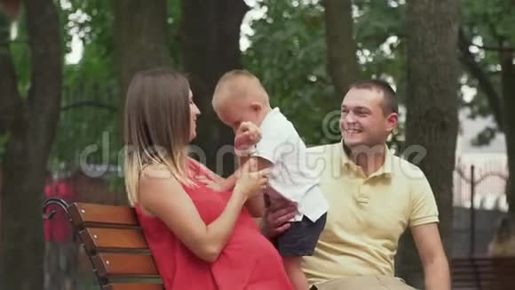 年轻的父母和一个小儿子坐在公园的长椅上视频的预览图