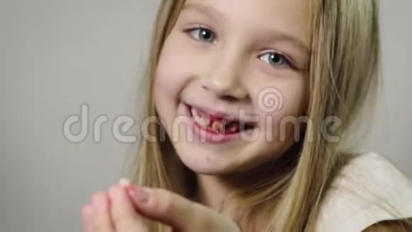 一个可爱的微笑女孩一个孩子她手里拿着一个撕裂的奶方和一个流血的牙龈下巴在一个房间里视频的预览图