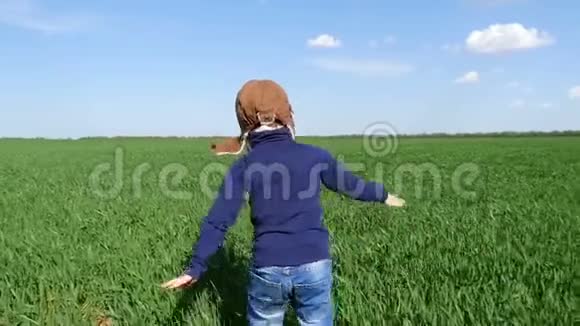 一个穿着飞行员制服快乐的孩子沿着绿色的田野奔跑双手伸向一边展示着飞行的景象视频的预览图