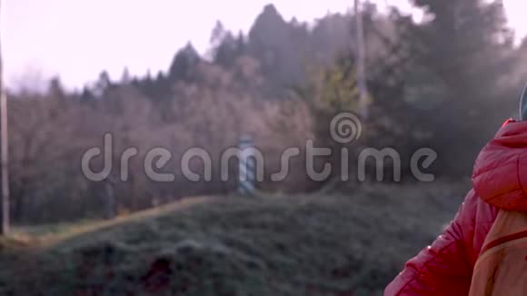 穿着红色夹克和橙色小背包的漂亮女徒步旅行者在寒冷的清晨站在树林里呼吸视频的预览图