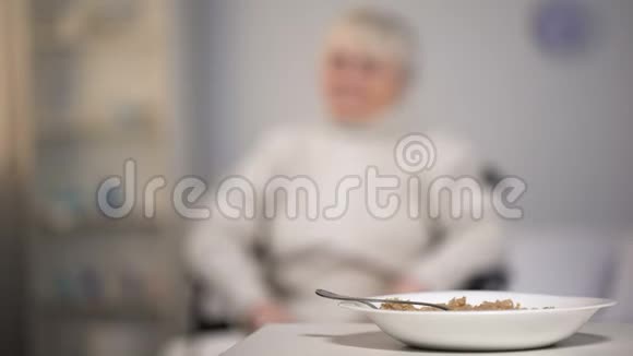 坐在轮椅上的悲伤的老妇人在医疗中心看着不美味的晚餐悲伤视频的预览图