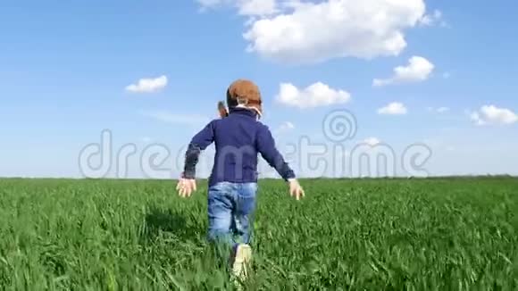 一个快乐的孩子穿着飞行员西装沿着绿色的田野奔跑视频的预览图