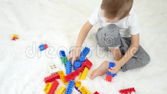 一个小可爱的男孩从设计师的彩色积木上搭起来坐在白色的地板上小孩坐在上面玩视频的预览图