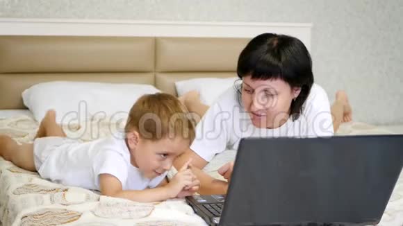 幸福家庭母亲和儿子躺在床上用笔记本电脑视频的预览图