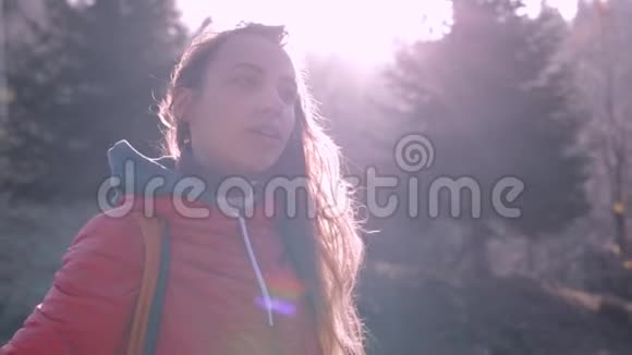 穿着红色夹克和橙色小背包的漂亮女徒步旅行者在寒冷的清晨站在树林里呼吸视频的预览图