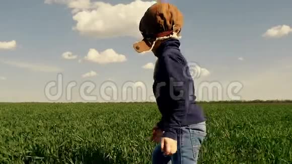 一个穿着飞行员西装快乐的孩子沿着一片绿色的田野奔跑双手伸向一边显示着一个飞行的人视频的预览图
