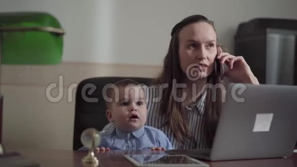 可爱忙碌的年轻母亲在家里工作抱着孩子那个女人在打电话而她的儿子视频的预览图