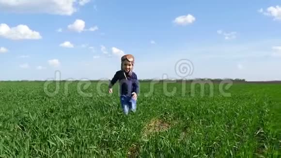 一个穿着飞行员西装快乐的孩子沿着绿色的田野跑着笑照相机的移动视频的预览图