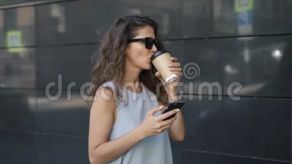 美丽的年轻女子喝着咖啡在灰色的墙边上网视频的预览图