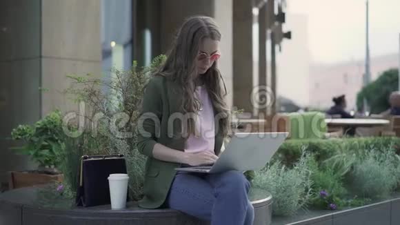 严肃的女商人在夏天的咖啡馆里用笔记本电脑工作喝咖啡视频的预览图