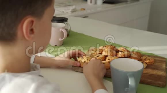 男孩在现代厨房吃早餐男孩吃带牛奶的饼干厨房里的白色桌子灰色碗在桌子上关门视频的预览图