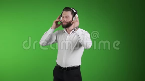 年轻英俊的男人在绿色工作室背景下与世隔绝听音乐在耳机上微笑快乐去跳舞吧视频的预览图