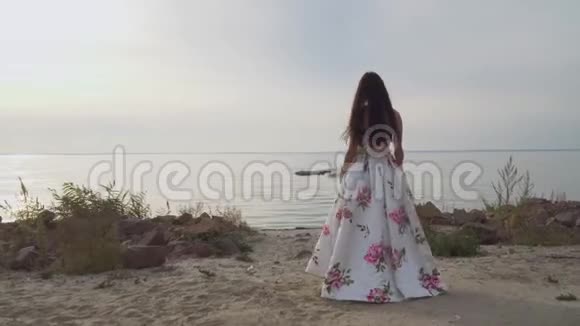 穿着一件漂亮长裙子的漂亮女孩走在河边视频的预览图