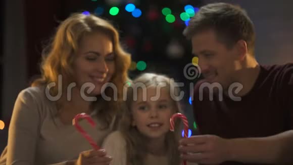 一家人拿着糖果靠近闪闪发光的树和灯圣诞节的传统视频的预览图