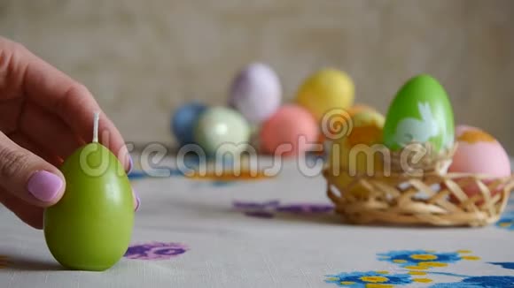 女人的手在桌子上放了三支复活节蜡烛绿色橙色和黄色背景中五颜六色的复活节彩蛋视频的预览图