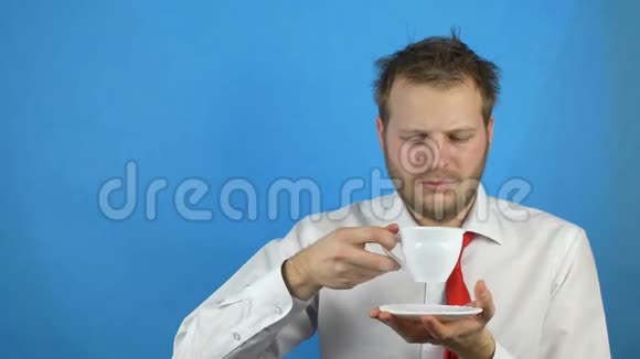 一个留着胡子的年轻人穿着白衬衫打着领带喝着咖啡昏昏欲睡背景是蓝色视频的预览图