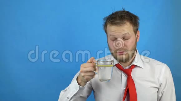 年轻的白种人男性商人穿着白衬衫打着宿醉领带喝着柠檬水昏昏欲睡蓝色背景视频的预览图