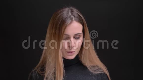 年轻的白种人长发金发的金发女孩在黑色背景下挑逗地观看镜头的肖像视频的预览图