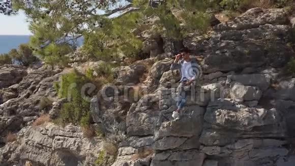 青年旅行者在海边的岩石悬崖上的鸟瞰图视频的预览图