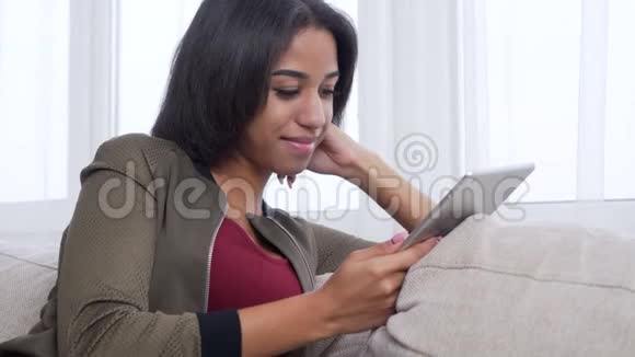在沙发上使用数字平板电脑欣赏媒体内容的少女视频的预览图