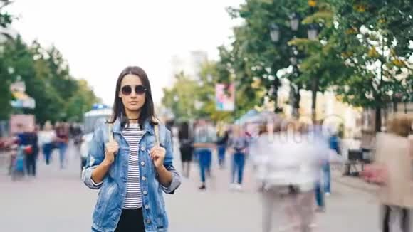 一张自信的年轻女士戴着太阳镜站在市中心的跑步人群中休息的照片视频的预览图