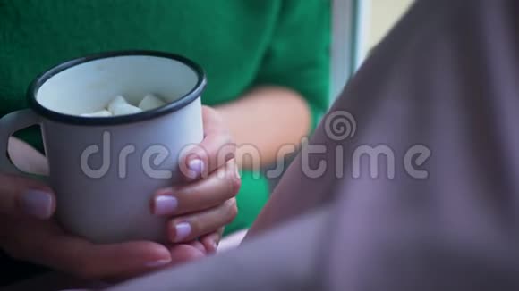 穿绿色针织毛衣的女人拿着一个铁杯坐在窗户上视频的预览图