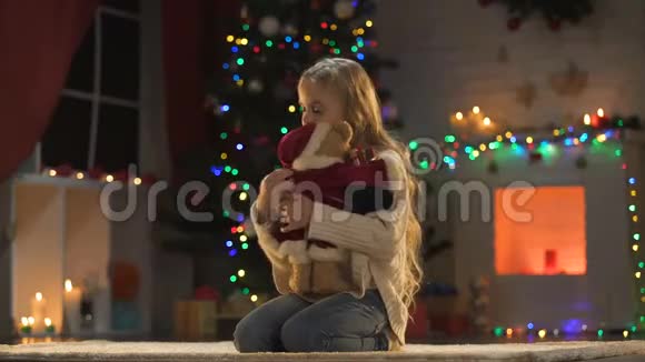 孤独可爱的女孩坐在闪闪发光的圣诞树和花环附近想念父母视频的预览图