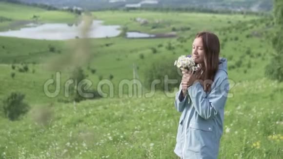 穿着雨衣的年轻女子带着鲜花走在田野上视频的预览图