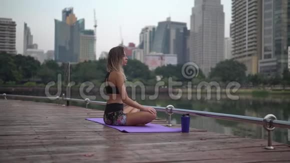 运动女性在城市公园湖边健身地毯上锻炼后放松视频的预览图