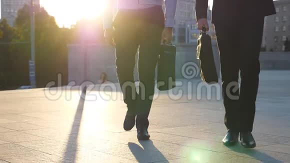 日落时分两个商人的脚带着公文包在城市街道上散步合作伙伴一起上下班视频的预览图