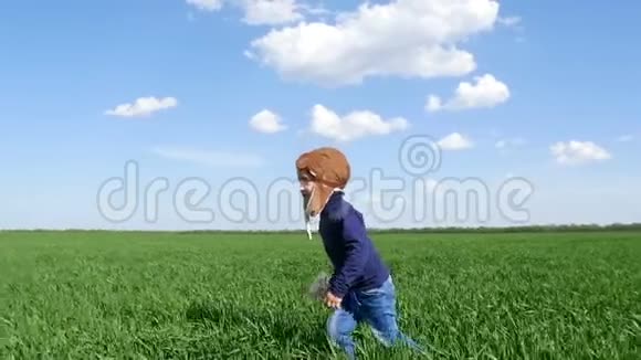 一个穿着飞行员西装的快乐孩子慢节奏地沿着绿色的田野和玩具飞机奔跑视频的预览图