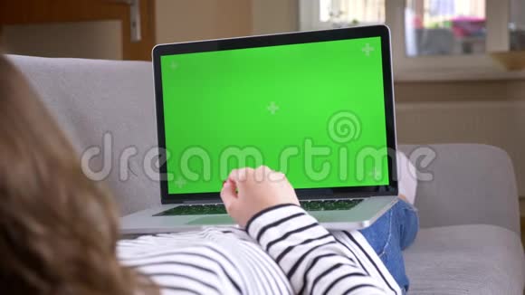 在一间舒适的公寓里在沙发上铺着绿色屏幕的笔记本电脑上拍摄女性打字的特写后景视频的预览图