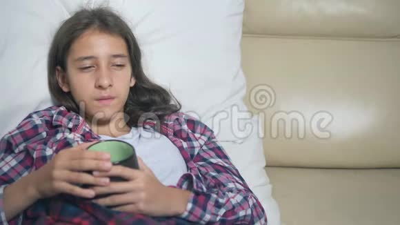 生病的少女在被窝里喝一杯热饮料视频的预览图