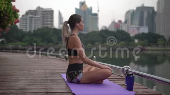 一位留着长发尾巴的女士在梅格波利斯市公园练完瑜伽后在健身地毯上放松视频的预览图
