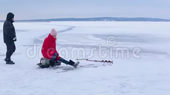 穿着红袄穿着毡靴的漂亮渔夫帮着冬天钓鱼视频的预览图