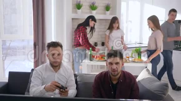 家庭聚会玩家朋友玩电子游戏喝啤酒女朋友在后台准备小吃视频的预览图