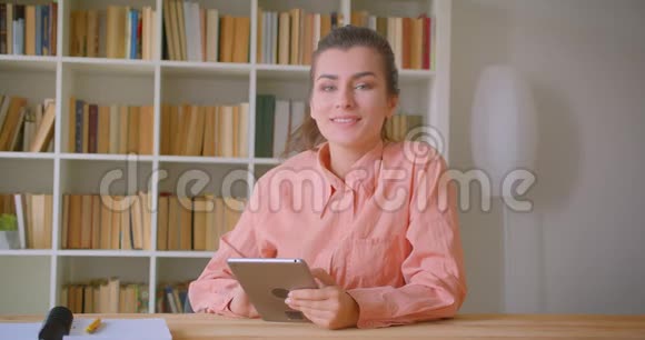 在大学里一位年轻迷人的女学生用平板电脑看着镜头开心地笑着特写照片视频的预览图