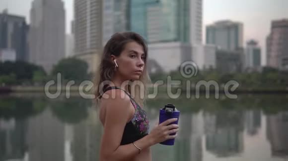 有气脚的女人在城市公园的高楼上锻炼后从健身蓝杯中喝饮料视频的预览图