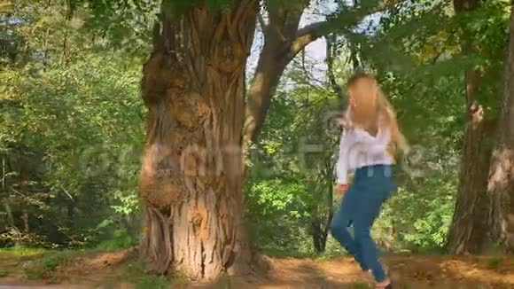 在运动中拍摄伟大的金发白种人女孩在绿色的夏季公园跳舞温暖的天气美丽的视频的预览图