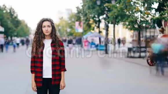 当人群拥挤时孤独的女孩站在市中心的人行道上看着镜头穿着休闲服装视频的预览图