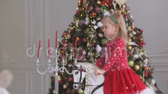 一个小女孩正在荡秋千坐在一个有圣诞装饰和装饰圣诞树的房间里的玩具马上视频的预览图