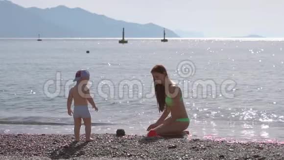 年轻女子在海边的沙滩上慢动作地和儿子玩耍视频的预览图