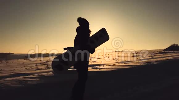 剪影女孩滑雪板行走与滑雪板在山顶在日落视频的预览图