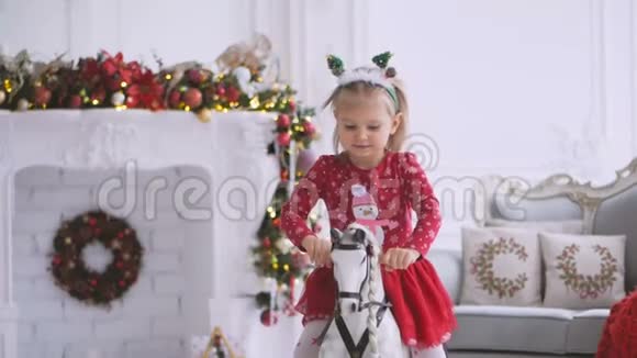 一个小女孩正在荡秋千坐在一个有圣诞装饰和装饰圣诞树的房间里的玩具马上视频的预览图