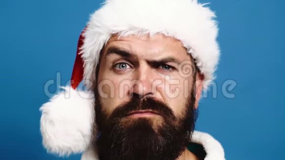 一个戴着一顶新年帽子的留着胡子的男人的特写在蓝色背景下引起了人们的眉毛新年概念圣诞老人把他视频的预览图